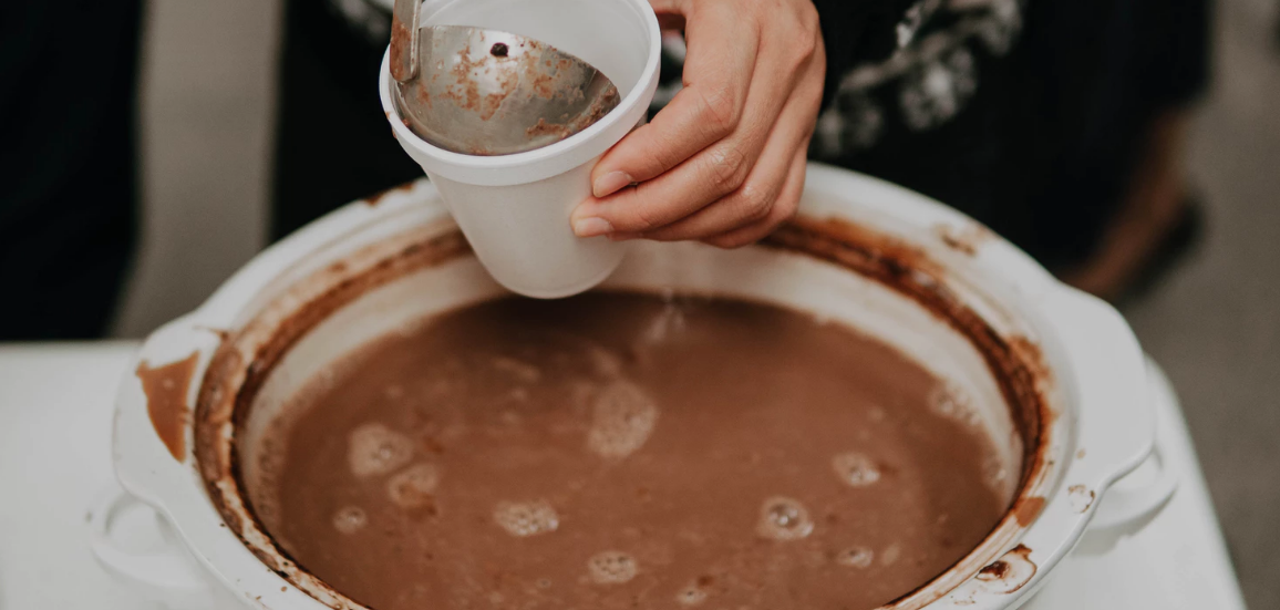 A person scooping out hot cocoa from a slow cooker